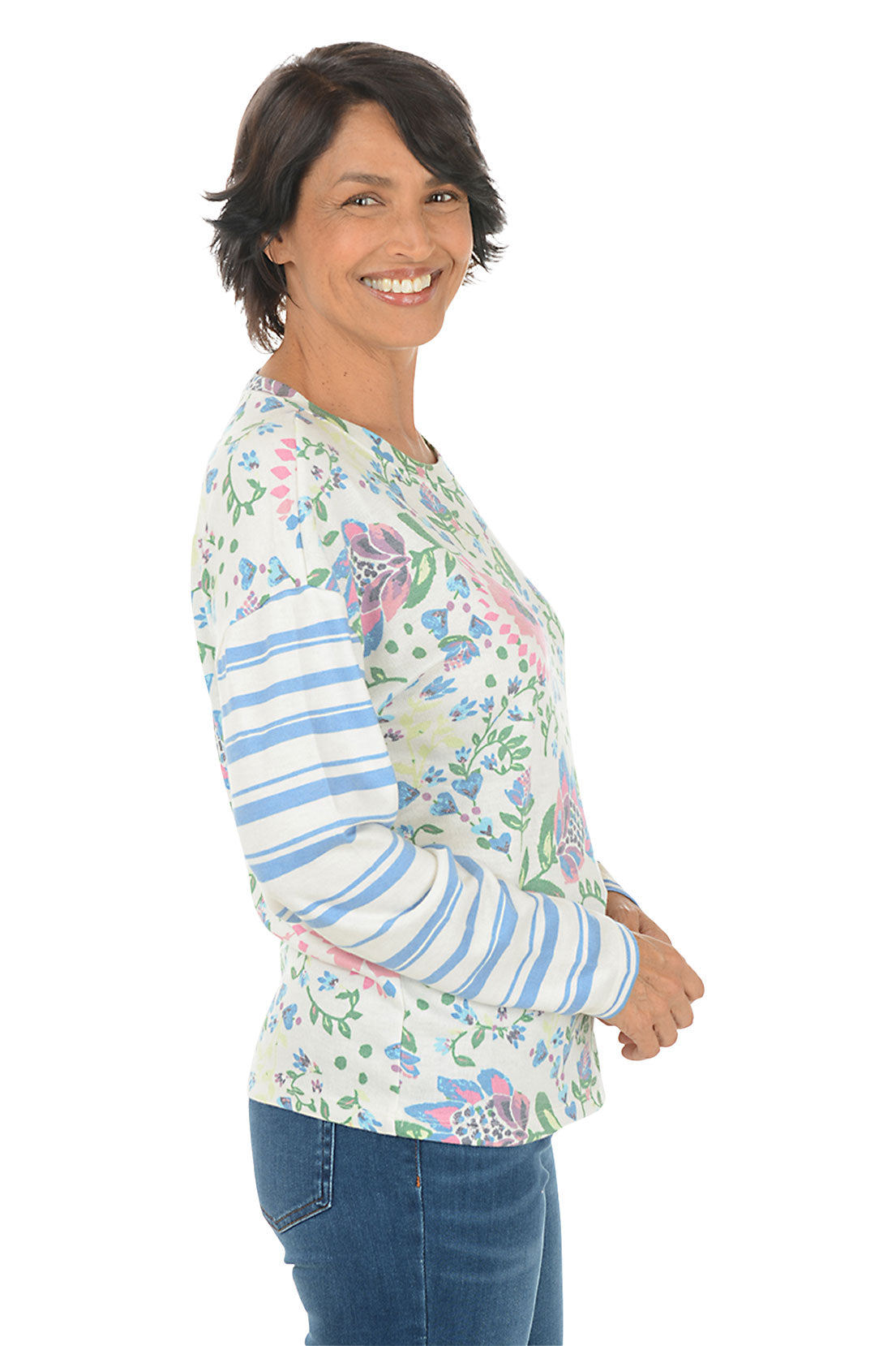 Woman wearing a floral long-sleeve shirt with blue jeans on a white background. Side shot.