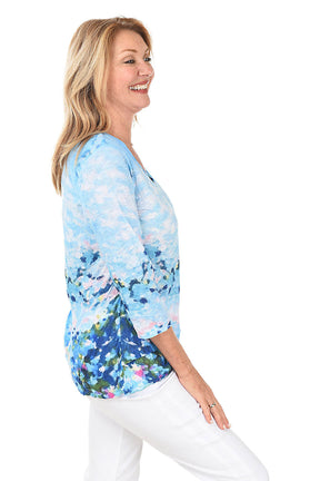 Woman wearing a blue floral long-sleeve top on a white background. Side shot.