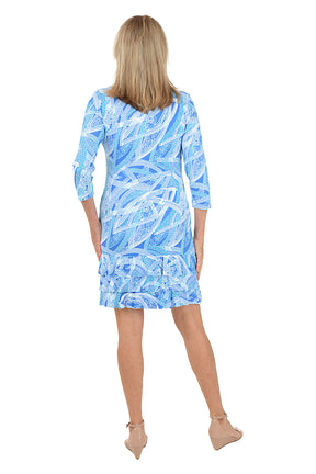 Woman wearing a blue patterned dress with a ruffled tiered hem on a white background. Back shot.