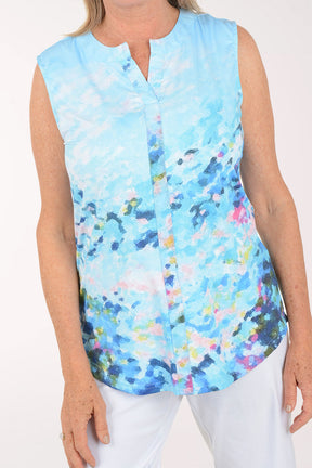 Woman wearing a sleeveless, light blue floral blouse with white pants on a white background