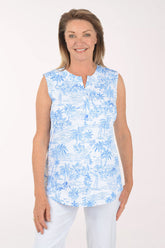 Woman wearing a blue floral sleeveless top and white pants on a white background