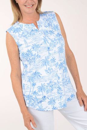 Woman wearing a blue floral sleeveless top and white pants on a white background