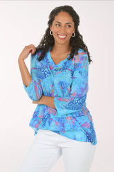 Woman wearing a blue patterned blouse with white pants on a white background