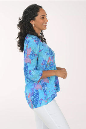 Woman wearing a blue patterned blouse with white pants on a white background