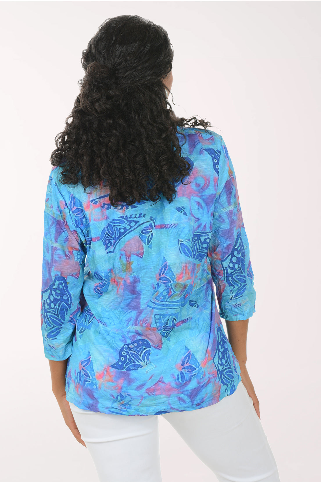 Woman wearing a blue patterned blouse with white pants on a white background