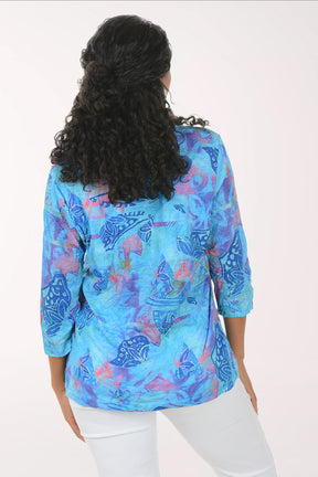 Woman wearing a blue patterned blouse with white pants on a white background