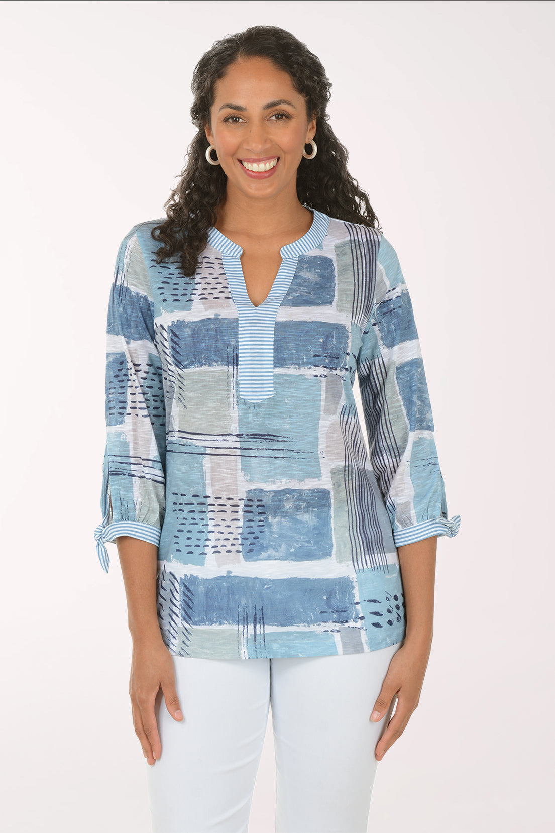 Woman wearing a blue patchwork blouse with white pants on a white background