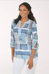 Woman wearing a blue patchwork blouse with white pants on a white background