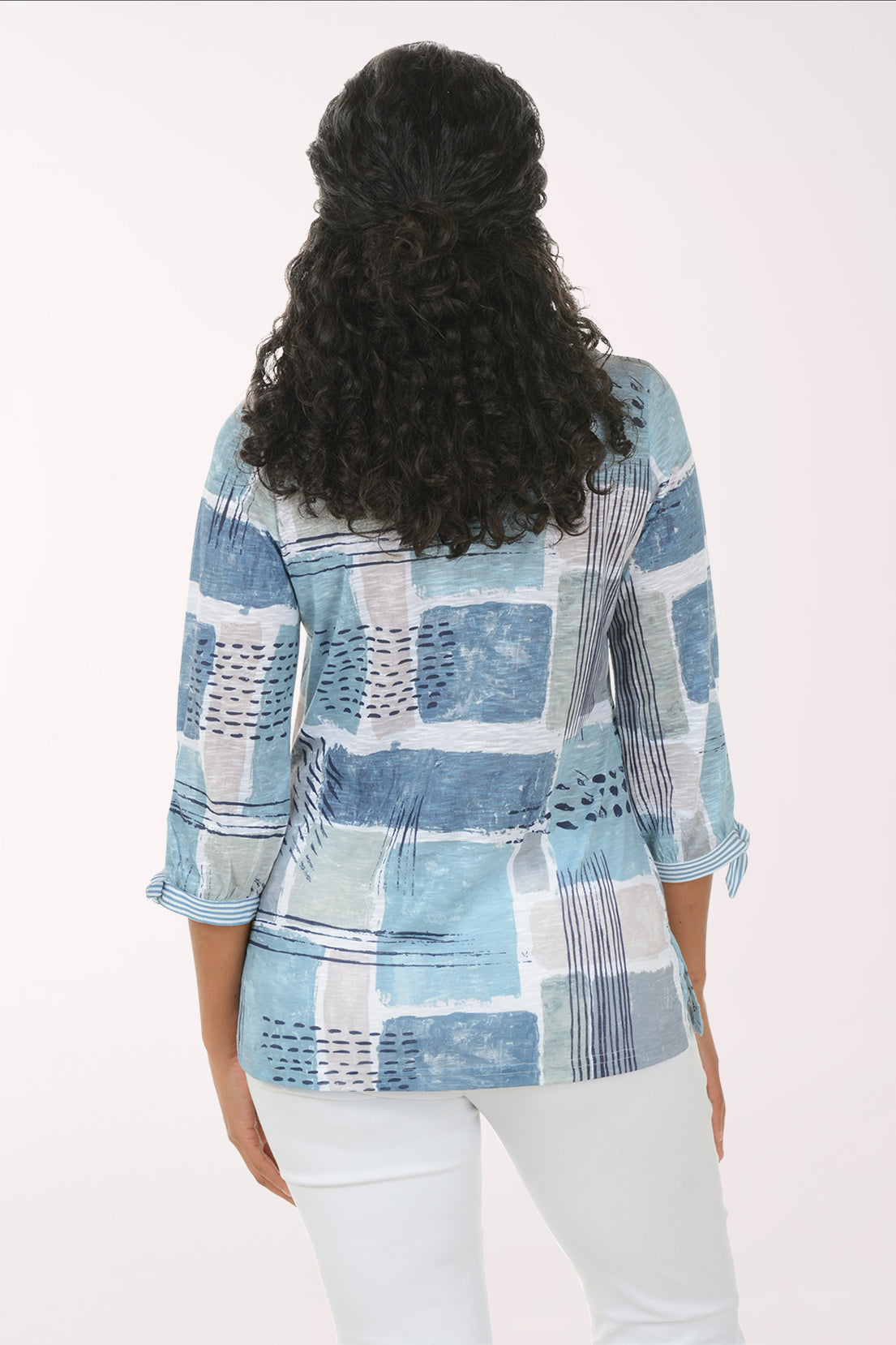 Woman wearing a blue patchwork blouse with white pants on a white background