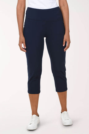 A woman wearing a navy capri pant and white sneakers against a light pink background