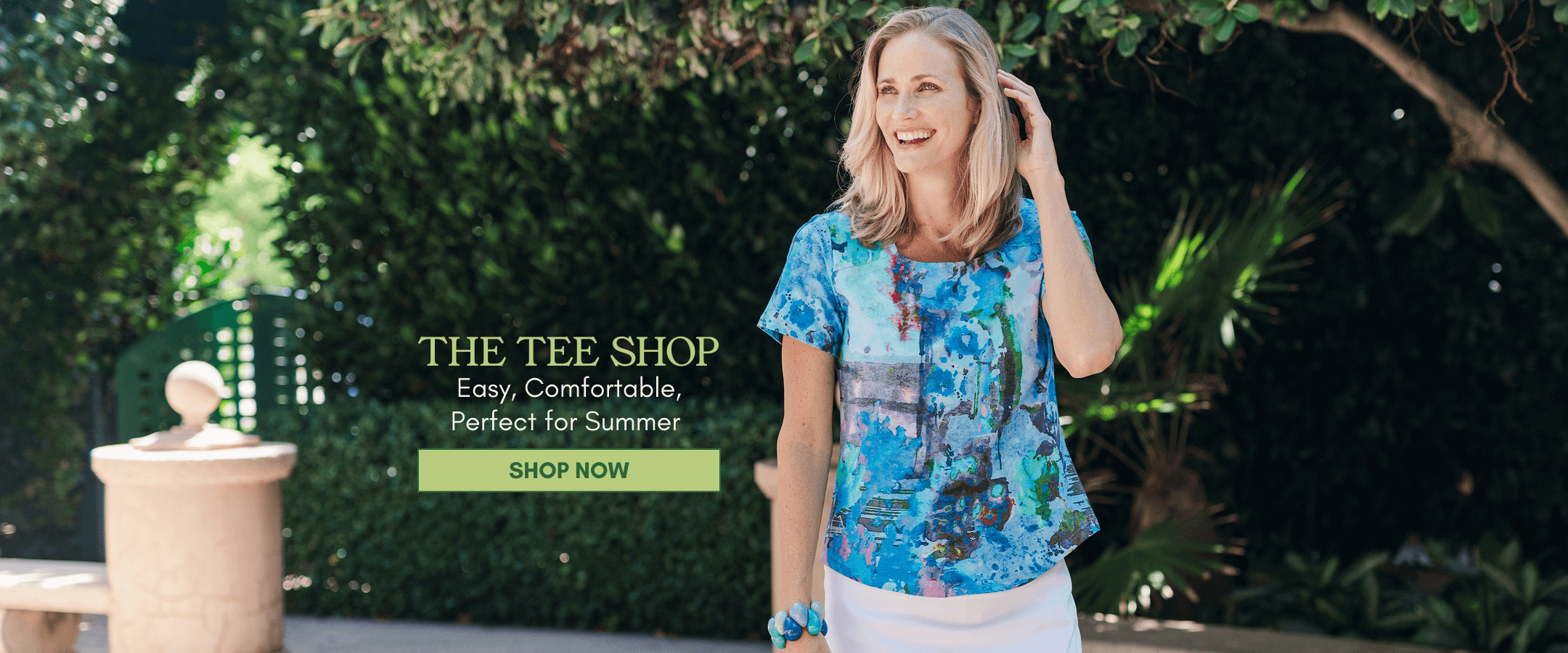 Model in tee posing in front of greenery. 