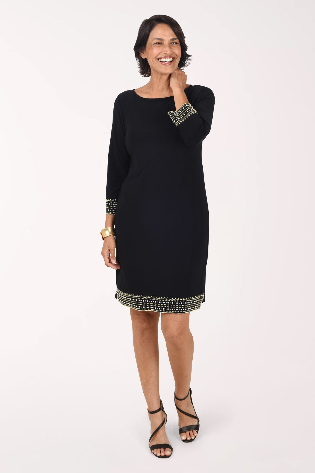 Front view of the black Beaded Trim dress with one hand at the shoulder, showing the beaded cuffs and the beaded band at the hem