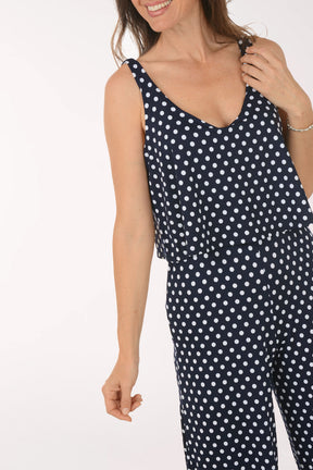 Woman wearing a navy blue jumpsuit with white polka dots on a white background