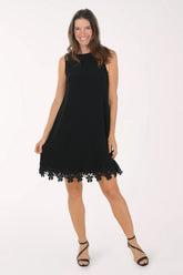 Front view of the black Tiana B Floral Lace Hem Sleeveless Dress, a sleeveless A-line dress with a rounded neckline and a border of black lace flowers along the above-the-knee hem, worn with black strappy heels