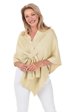 A woman wears a glittery gold wrapped shawl with a white pant against a white background.