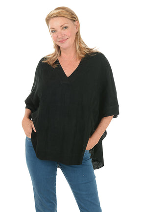 Woman wearing a black poncho and blue jeans on a white background.