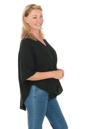 Woman wearing a black poncho and blue jeans on a white background. Side shot.