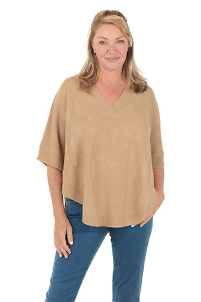 Woman wearing a beige sweater and blue jeans on a white background.