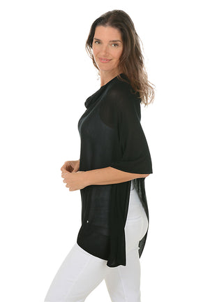 Woman wearing a black poncho and white pants on a white background. Side shot.