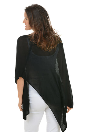Woman wearing a black poncho and white pants on a white background. Back shot.