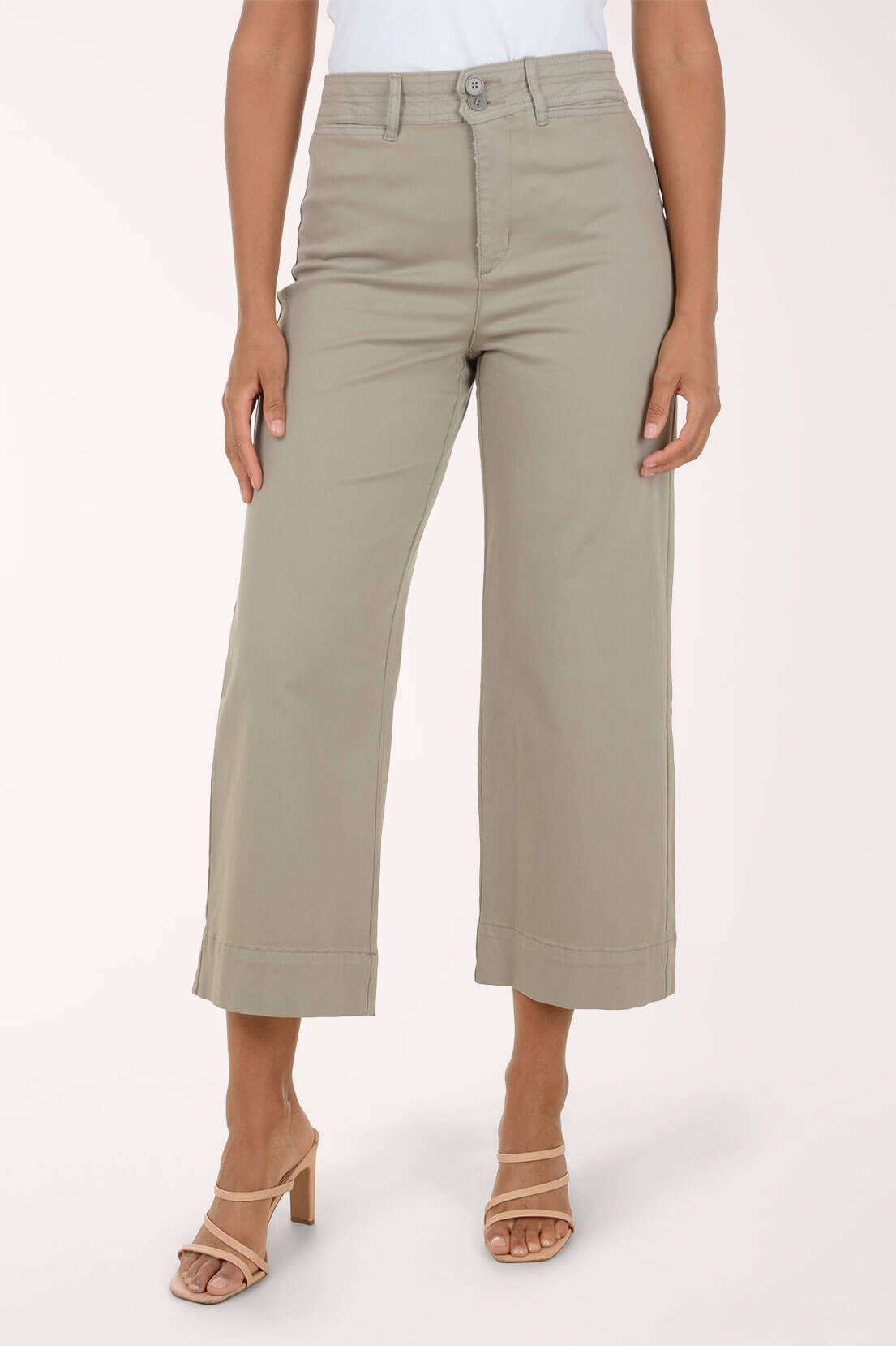A model wearing a pair of light sage green cropped pants with a rolled hem, paired with beige strappy high-heeled sandals, against a plain off-white studio background.