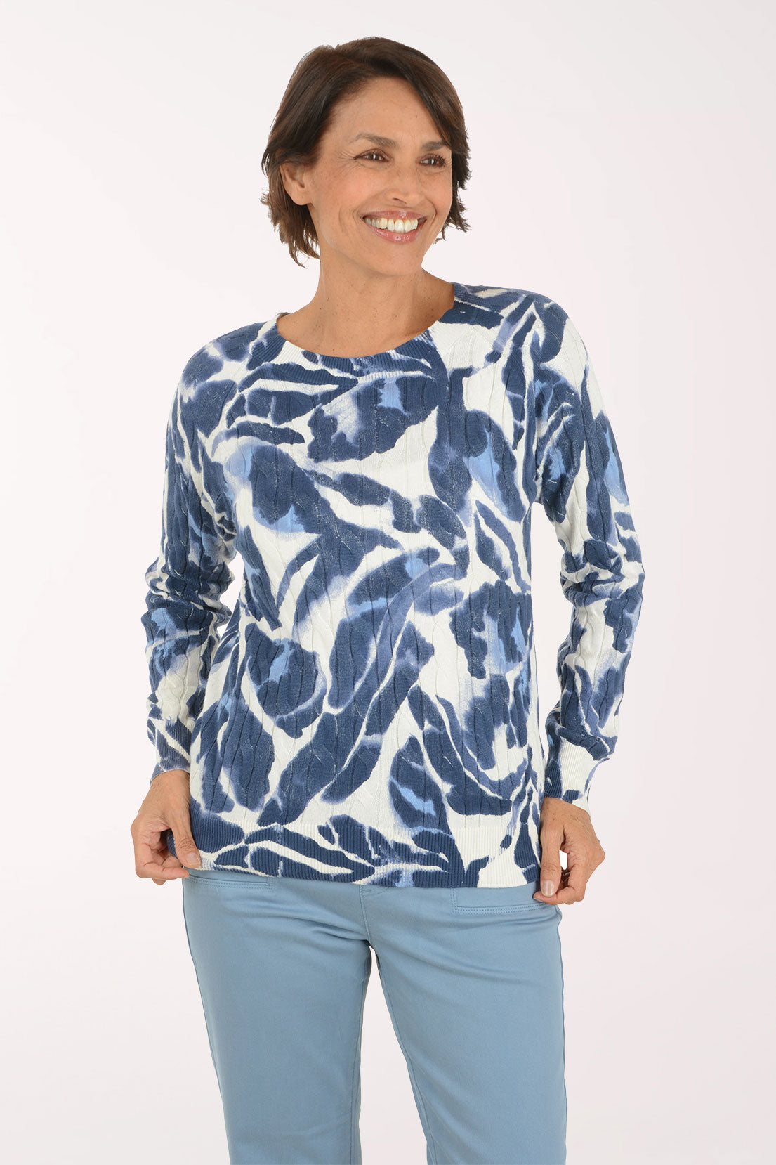 A woman modeling a long-sleeve top with a blue and white abstract pattern, paired with light blue pants, against a plain white studio background.