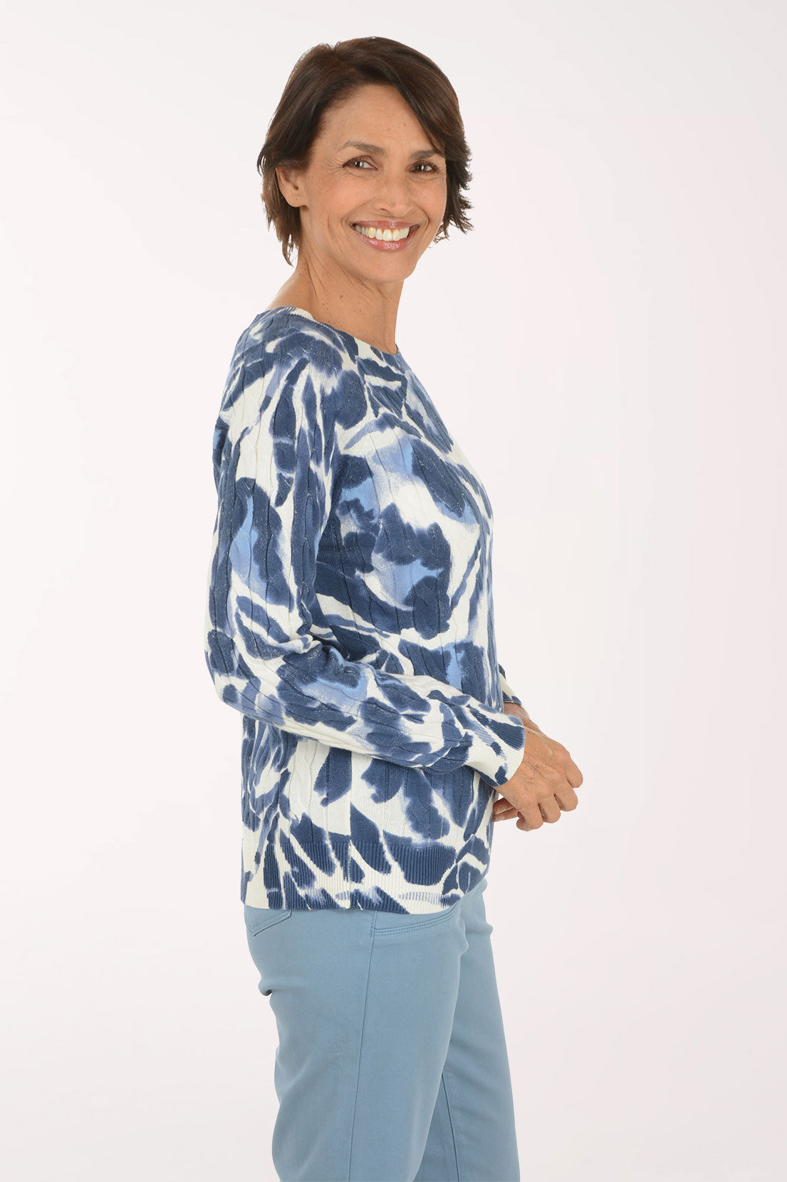 A woman modeling a long-sleeve top with a blue and white abstract pattern, paired with light blue pants, against a plain white studio background.