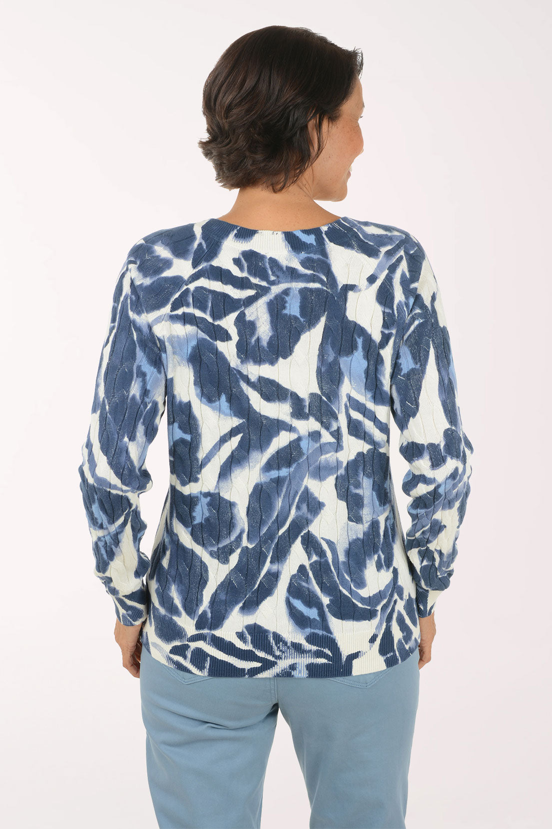 A woman modeling a long-sleeve top with a blue and white abstract pattern, paired with light blue pants, against a plain white studio background.