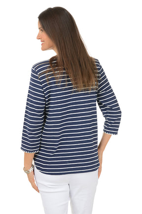 Woman wearing a navy and white striped shirt with white pants on a white background