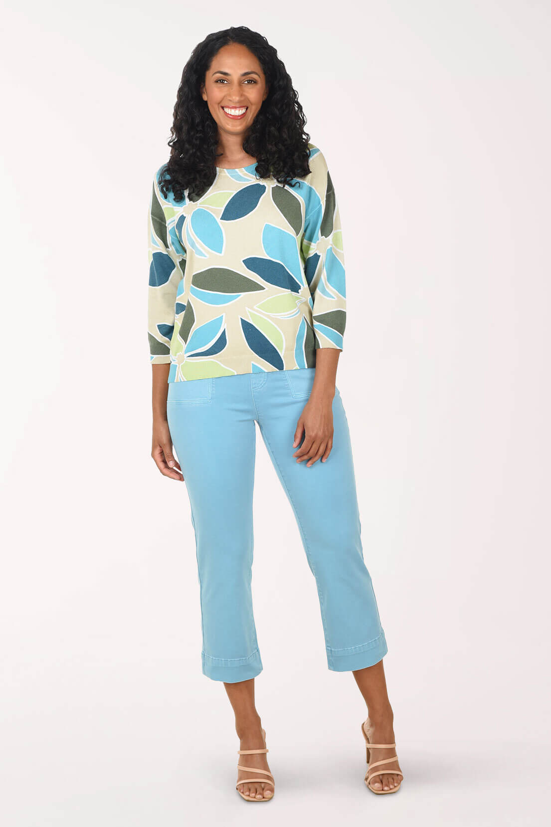 Woman wearing a patterned top and light blue pants on a white background