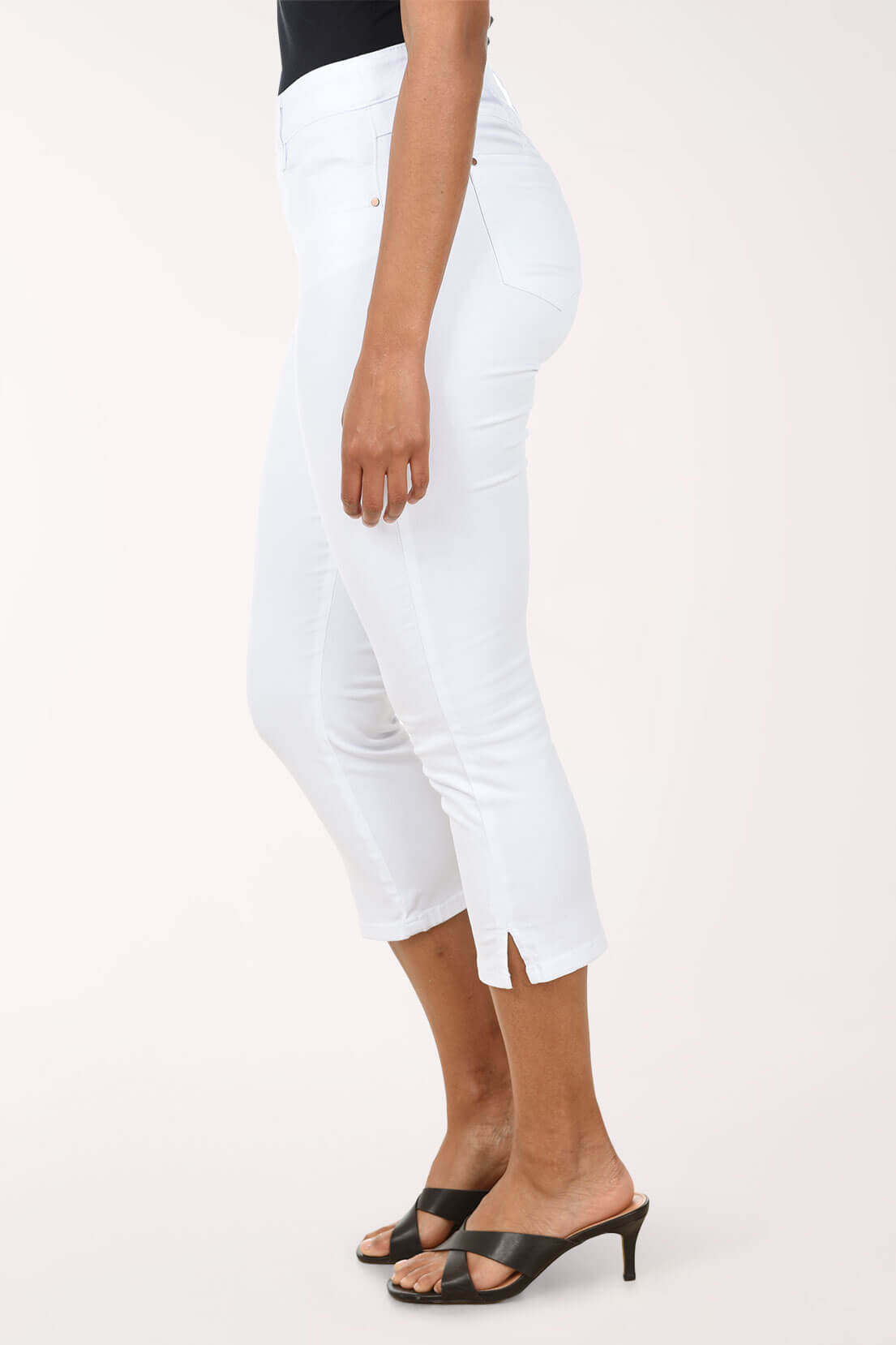 Woman wearing white capri pants against a light pink background. Side shot