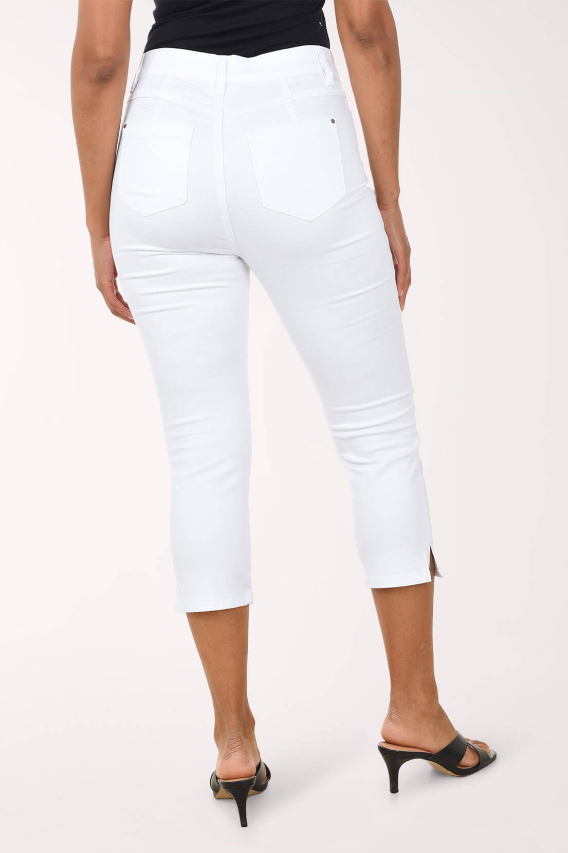 Woman wearing white capri pants against a light pink background. Back shot