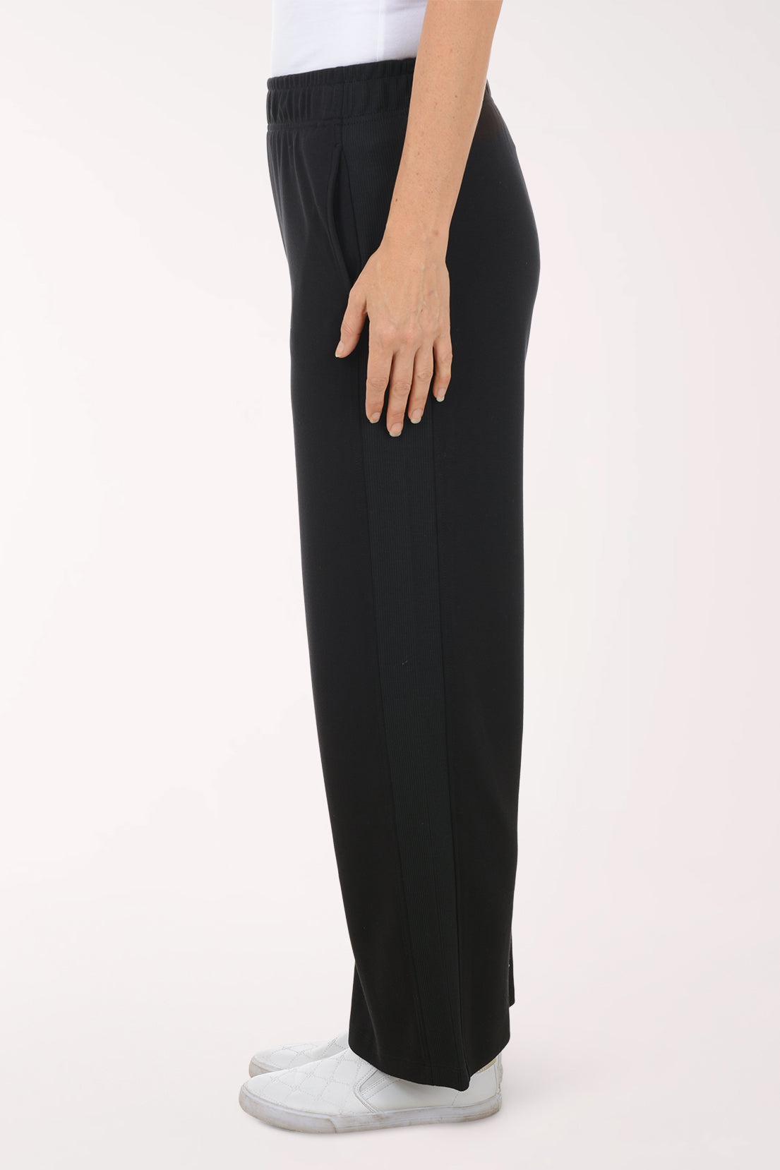 Person wearing black wide-leg pants and white shoes on a white background