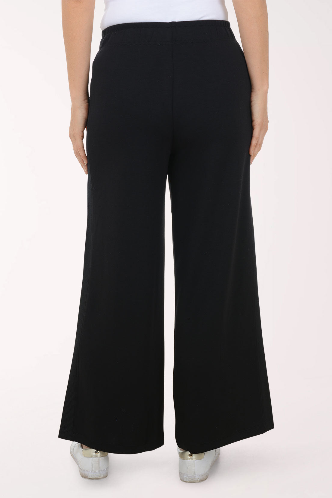 Person wearing black wide-leg pants and white shoes on a white background