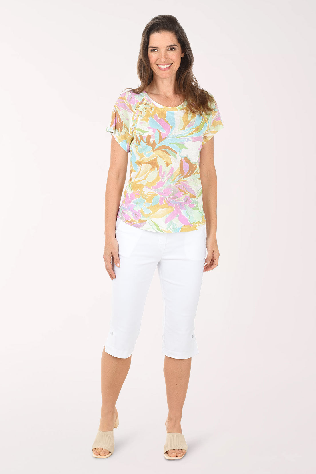Woman wearing a colorful floral top and white pants on a white background