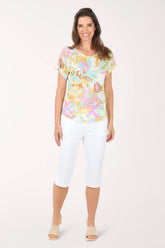 Woman wearing a colorful floral top and white pants on a white background