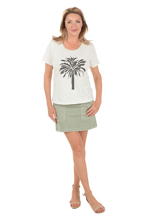 Woman wearing a white t-shirt with a palm tree design and a green skirt on a white background