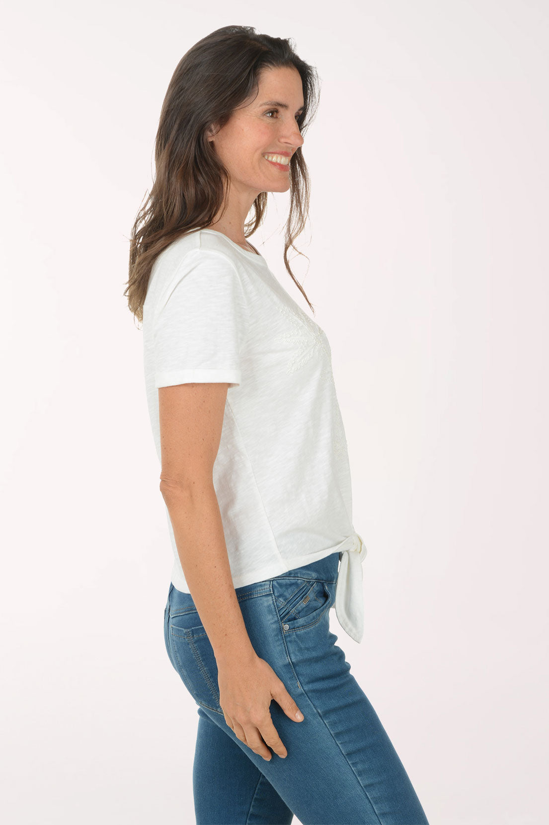 Woman wearing a white t-shirt with a tie detail and blue jeans on a white background
