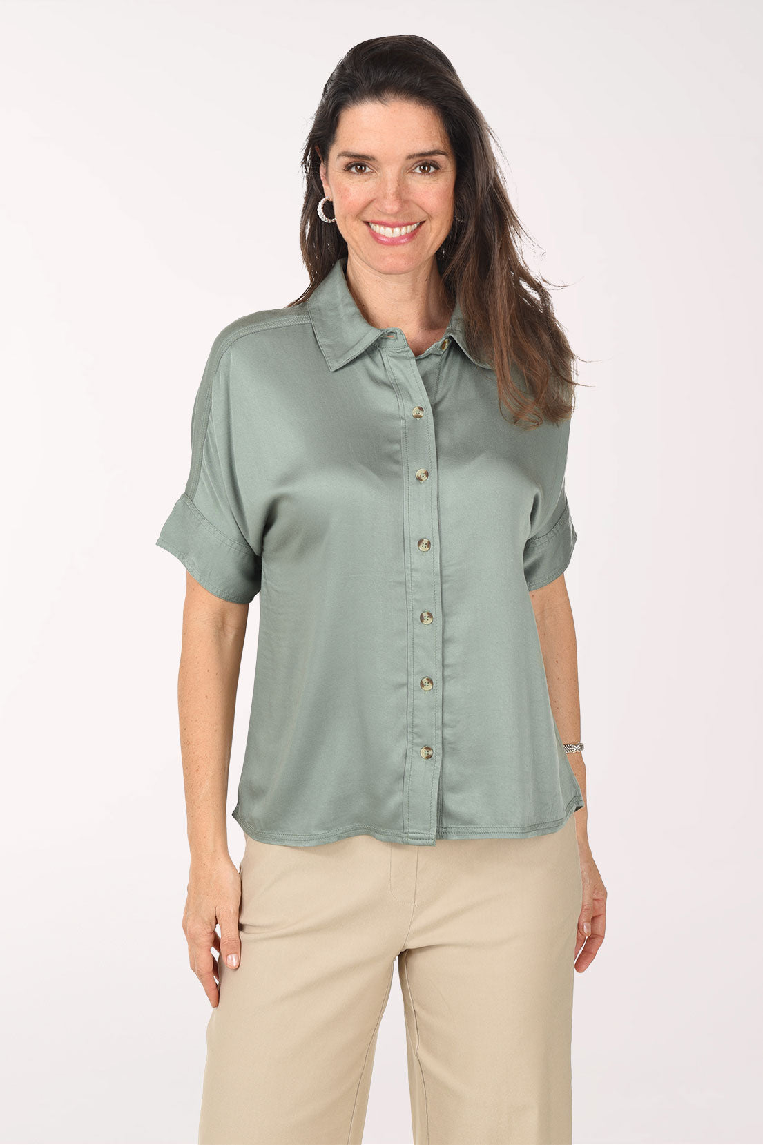 Woman wearing a light green button-up shirt and beige pants on a white background
