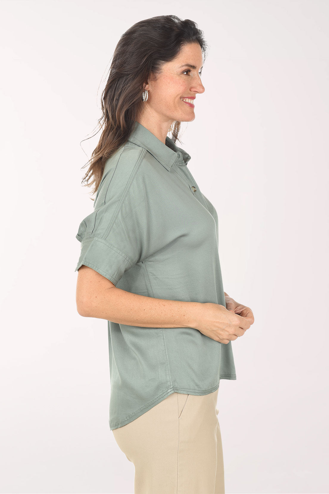 Woman wearing a light green button-up shirt and beige pants on a white background