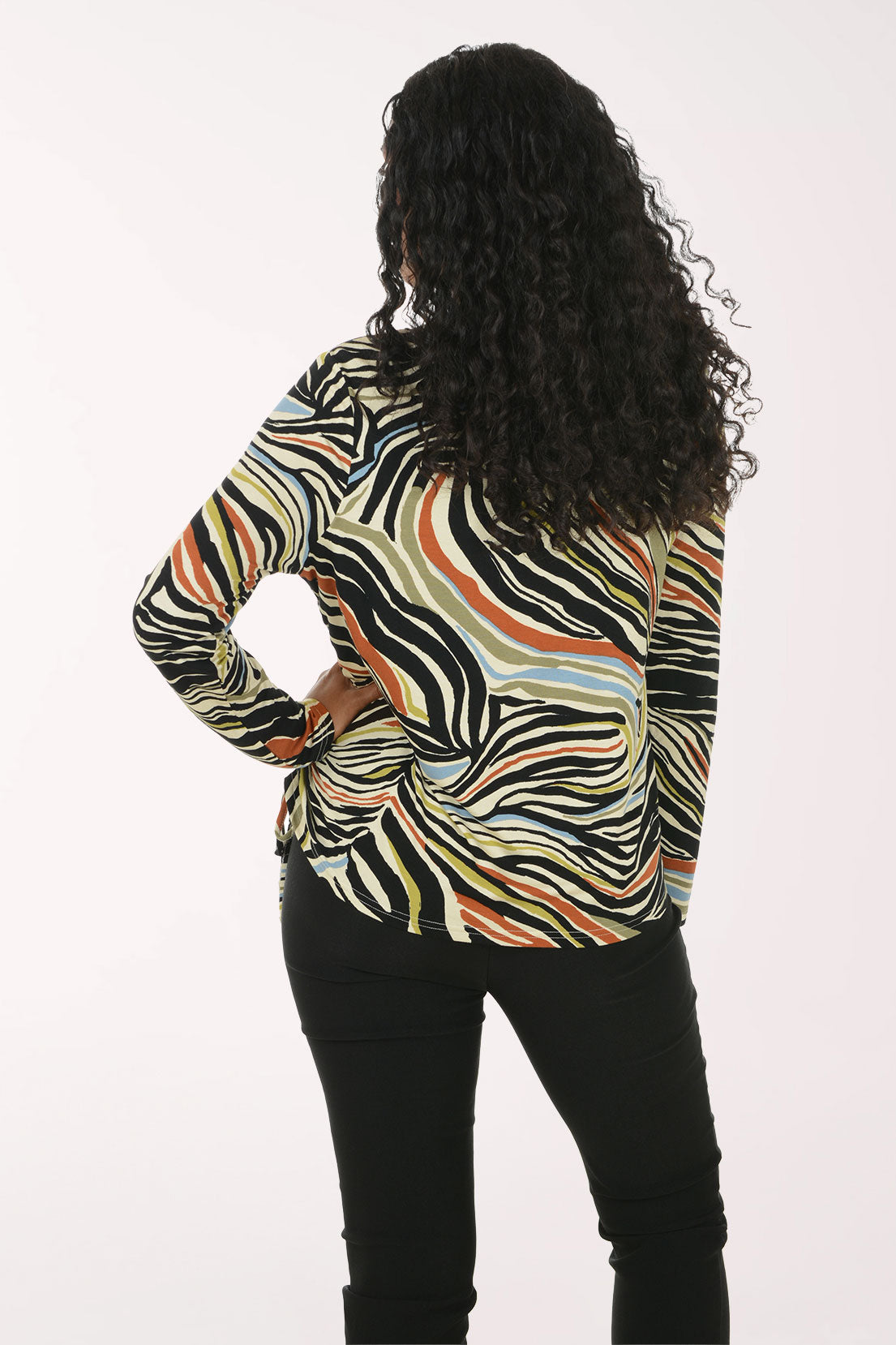 A woman modeling a long-sleeve top with a multicolor abstract wavy pattern in black, beige, orange, and white, paired with black pants, against a plain white background.