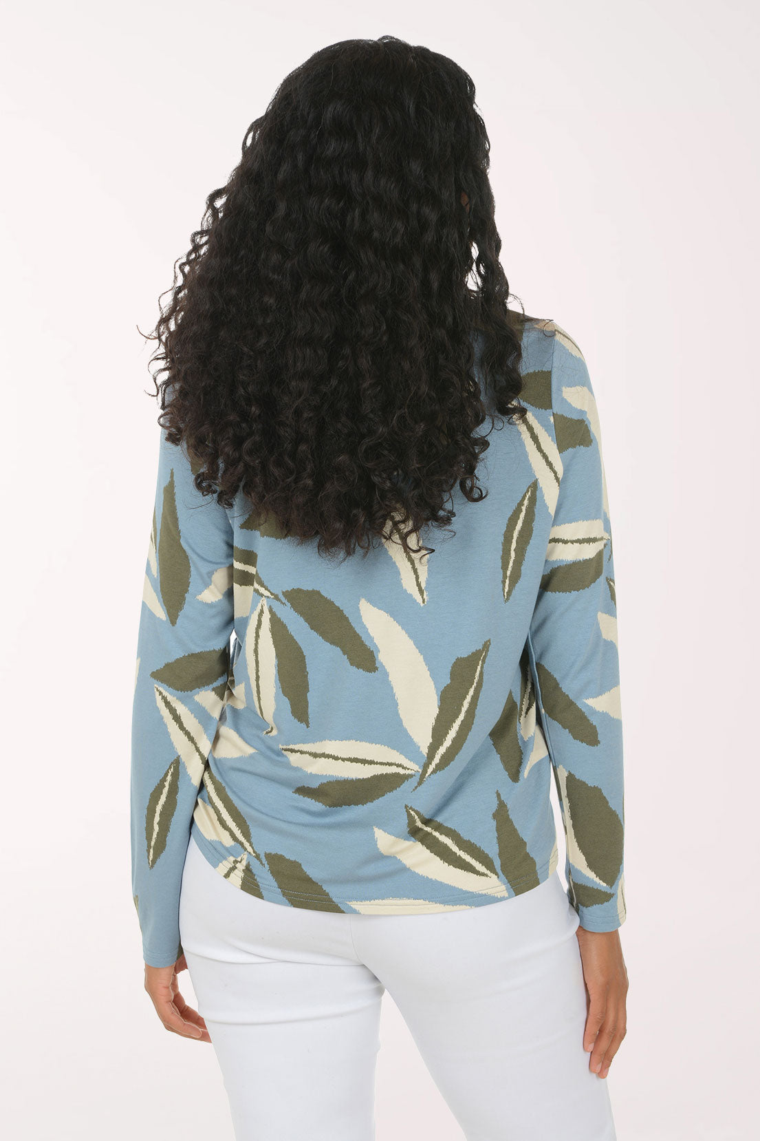 A woman modeling a light blue long-sleeve top with a green and beige leaf pattern, paired with white pants, against a plain white studio background.