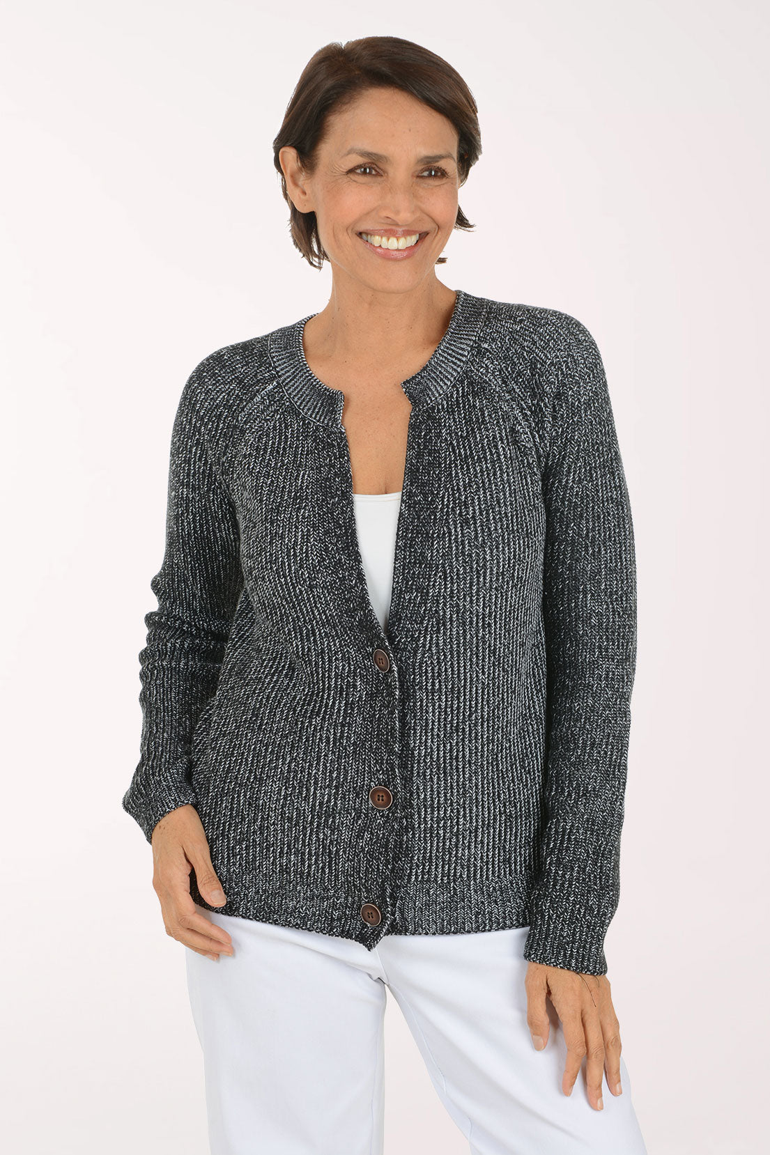 A smiling woman wearing a dark gray and black marled knit cardigan with brown buttons over a white top and white pants, photographed against a plain light background.