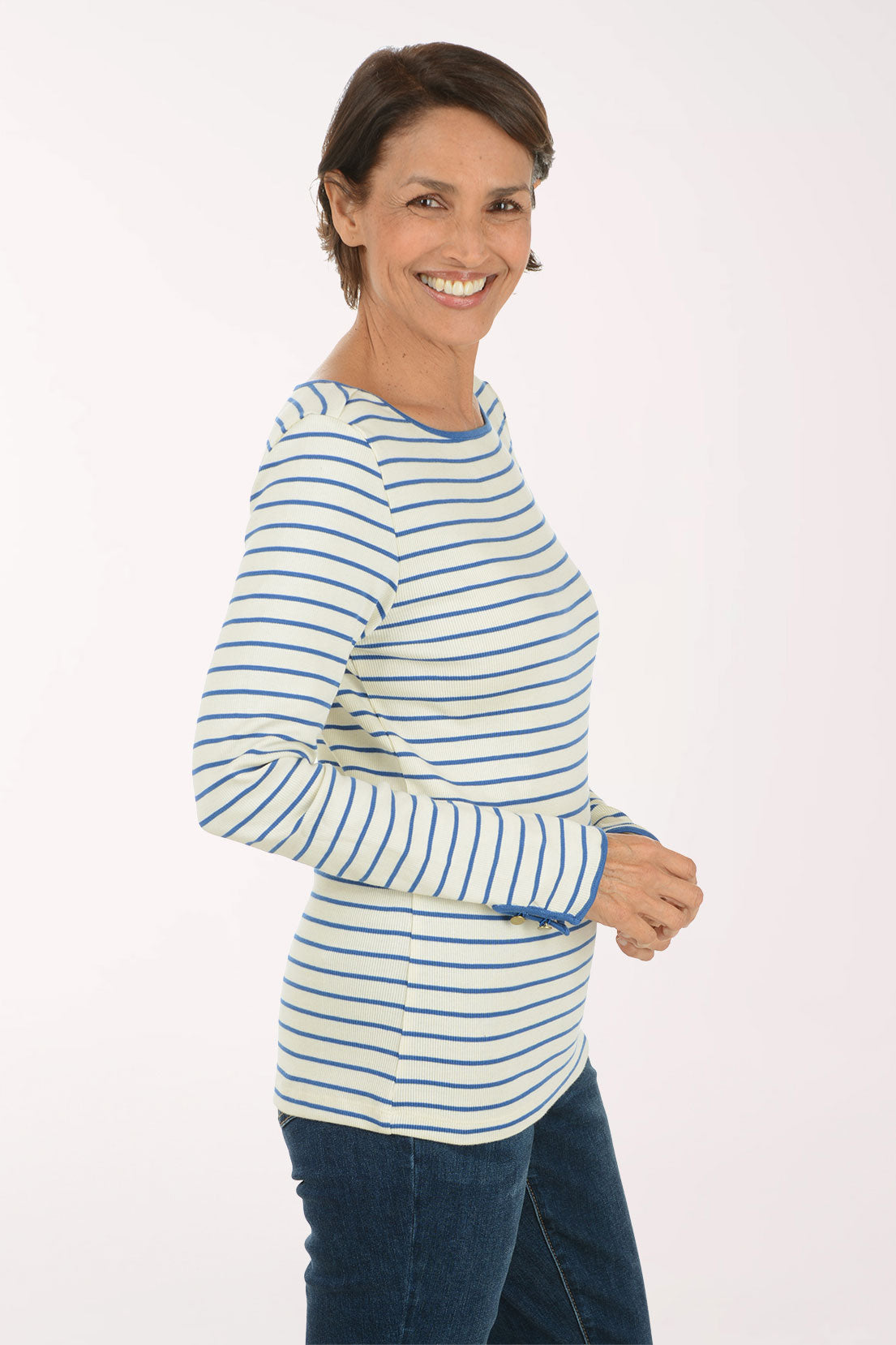 A woman modeling a long-sleeve striped top with blue and white horizontal stripes, paired with dark blue jeans, against a plain light background.