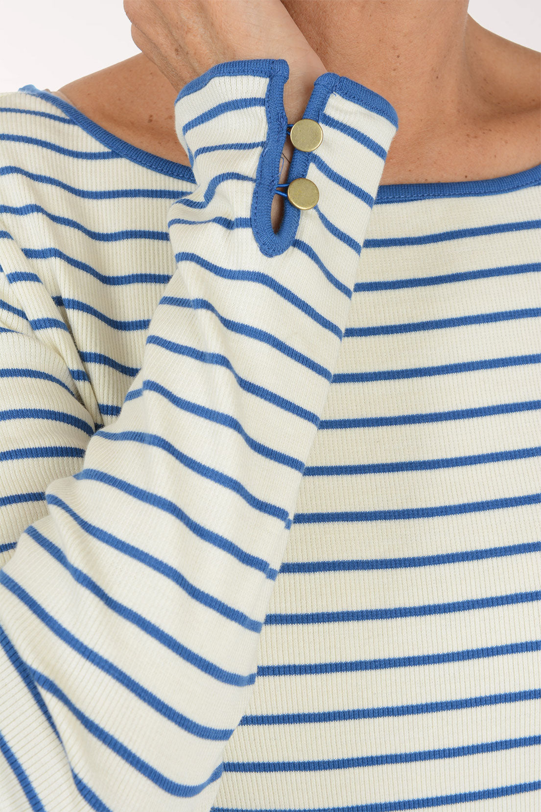 Close-up of a person wearing a ribbed long-sleeve top with blue and off-white horizontal stripes, featuring a buttoned cuff detail.