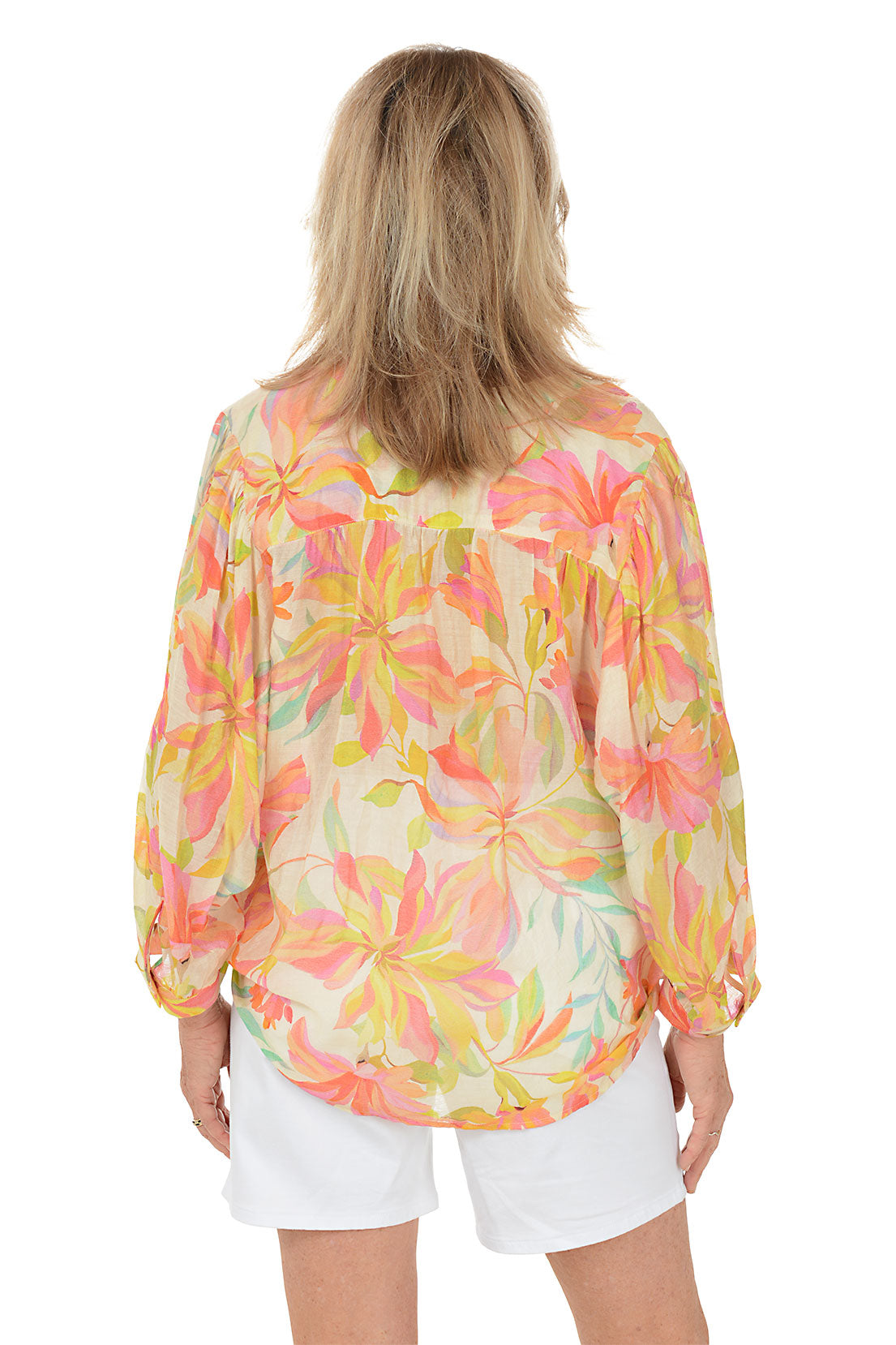 Woman wearing a colorful floral blouse and white shorts on a white background