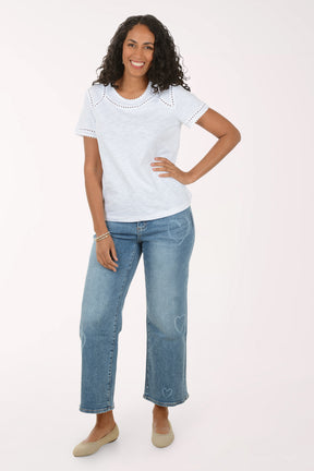 Woman wearing a white lace top and blue jeans on a white background