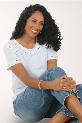 Woman wearing a white lace top and blue jeans on a white background