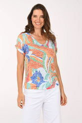 Woman wearing a colorful patterned top and white pants on a white background