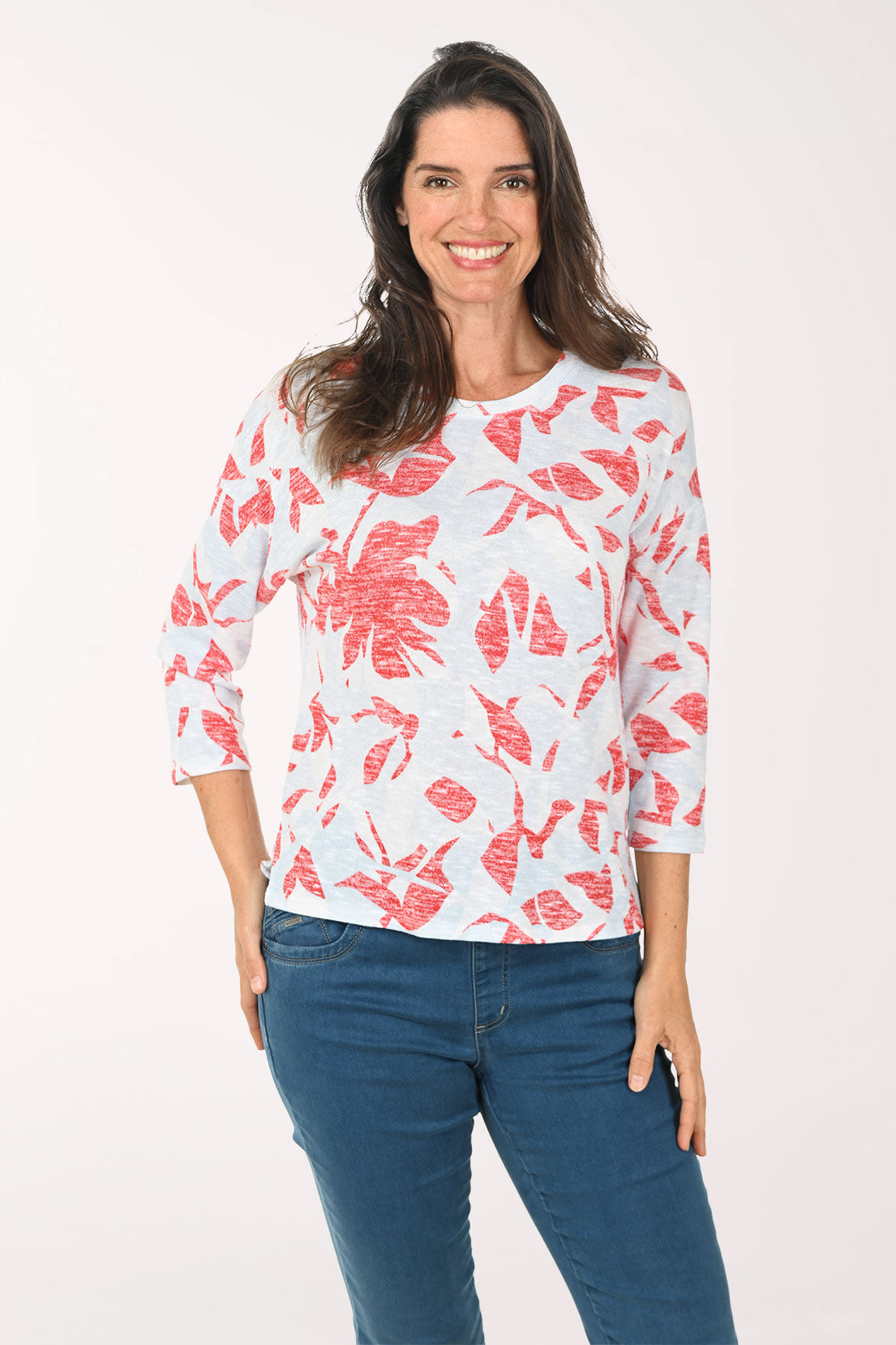 Woman wearing a white top with red floral pattern and blue jeans on a white background